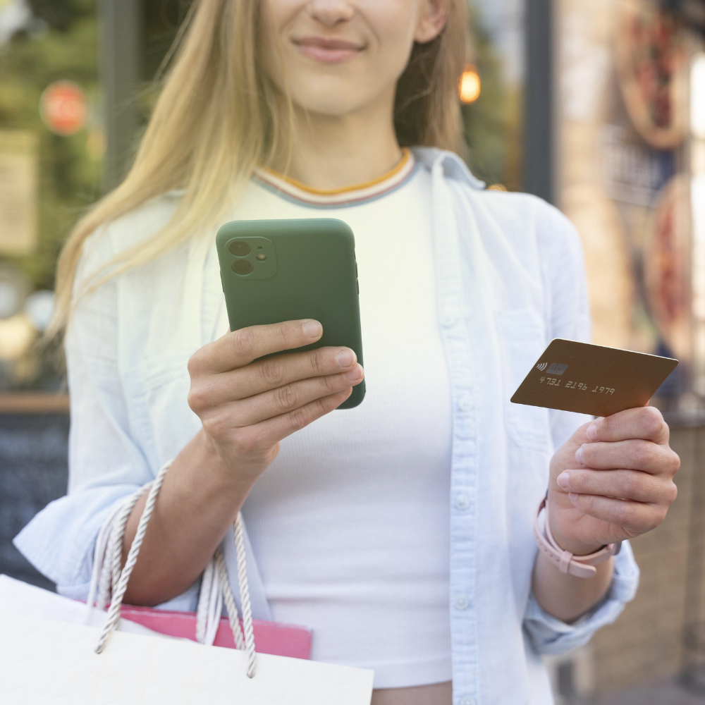 Mulher faz compras pelo celular usando cartão.