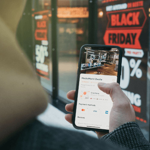 Homem aponta celular para promoção de black friday no e-commerce